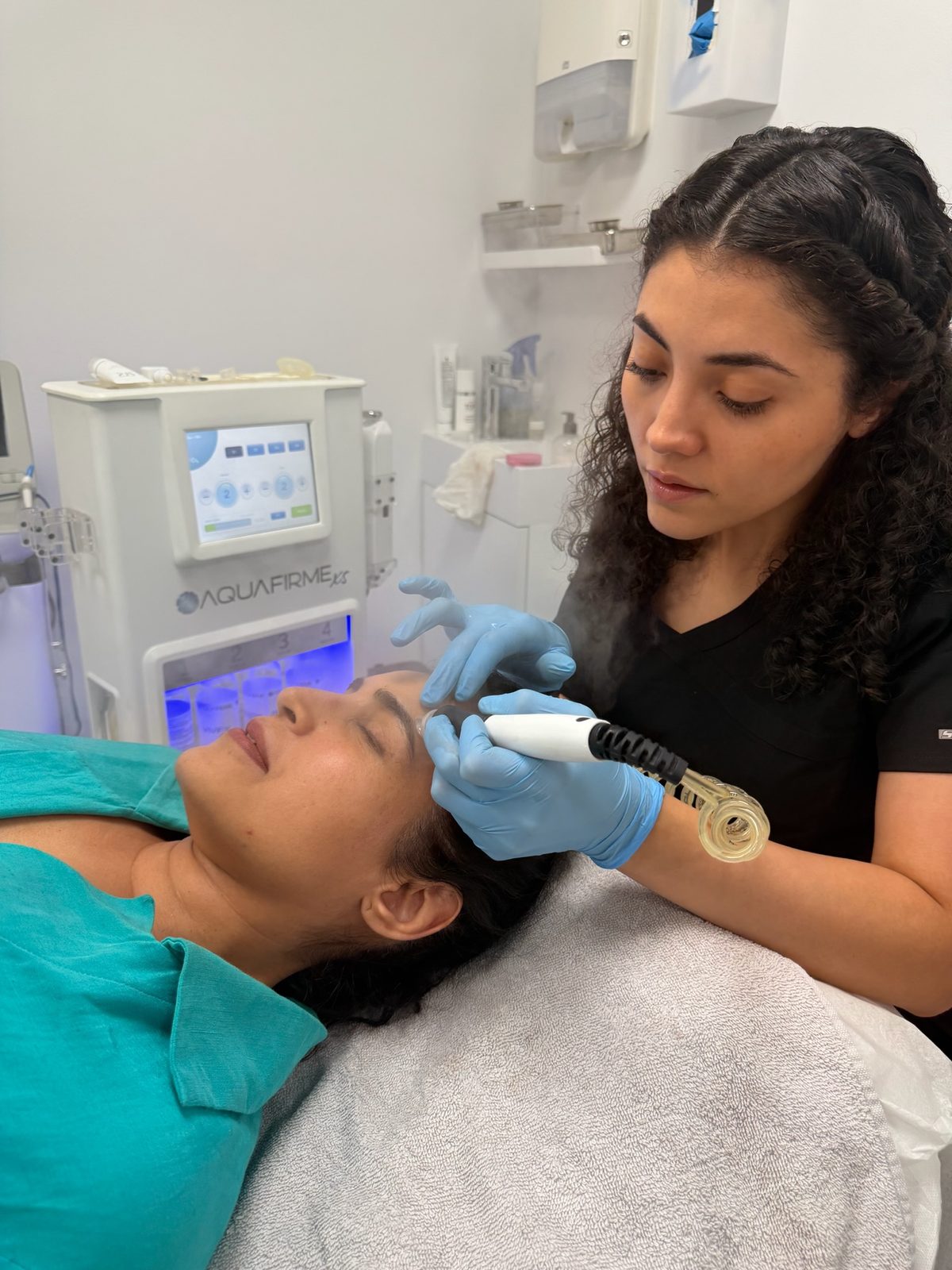 Shanelle performing an AquaFirme facial, guiding the handpiece along a client's brow